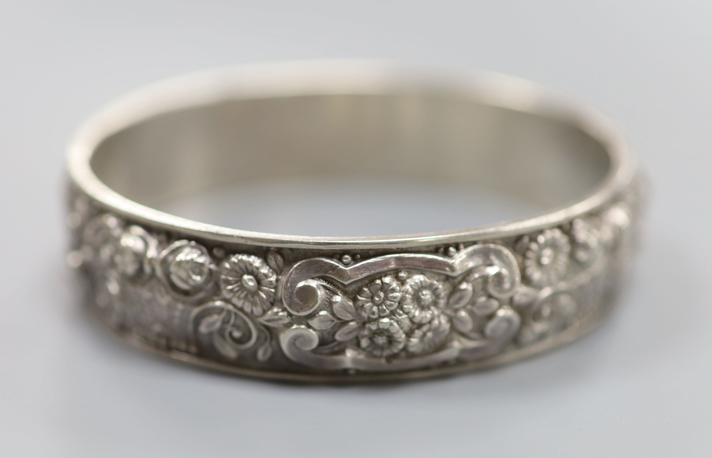 A continental white metal hinged bangle, decorated with continuous band of flowers and scrolls, 19 grams.